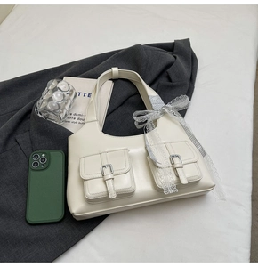 Dettaglio di una borsa sottobraccio bianco crema con fibbie decorative e fiocco in pizzo