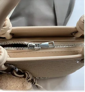 Close-up of a beige bucket bag showing smooth silver metal zipper and woven handle detail