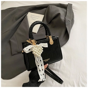 Detail van zwarte kunstlederen tas met geweven handvat, goudkleurige details en parelhanger