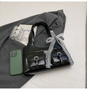 Dettaglio borsa tote nera con fiocco in pizzo su abito grigio e sfondo bianco