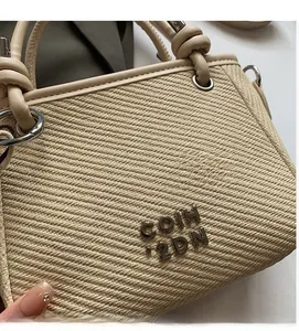 Close-up of beige woven bucket bag with silver metal logo and leather knot handle detail