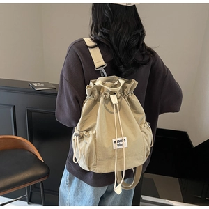 Detail of adjustable woven straps and drawstring closure on khaki nylon bucket backpack
