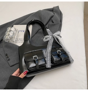 Dettaglio borsa tote in pelle lucida nera con fiocco in pizzo e tasche con fibbia in metallo