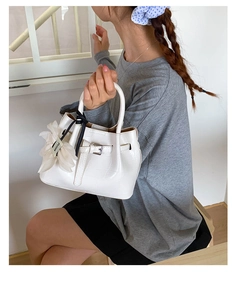 Detail der weißen Handtasche mit Krokodilprägung und elegantem Blumenanhänger aus Chiffon