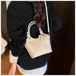 Close-up of a white bucket bag with pearl heart and lace bow on a black sweatshirt