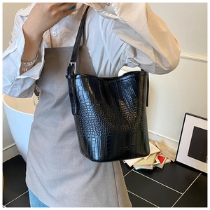 Detail view of black crocodile pattern leather bucket bag with slim shoulder strap