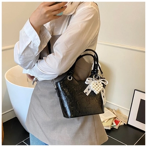 Detail of black glossy bucket bag with wrinkled texture and pearl lace bow charm