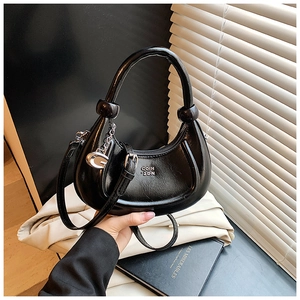 Detail view of black glossy crescent bag with gold G-charm and brand lettering