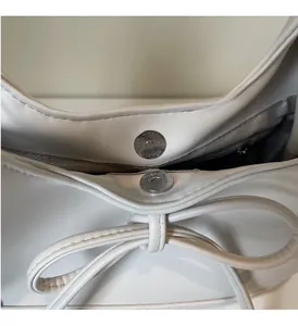 Detail of the magnetic metal clasp and bow decoration on a cream PU leather tote bag