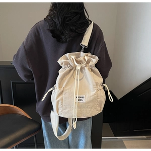 Detail view of the beige drawstring backpack showing the adjustable side pocket and straps