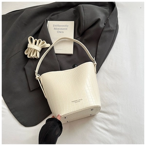 Detailed macro view of cream crocodile-embossed bucket bag with bottom silver studs
