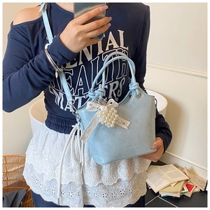 Detail of light blue bucket bag with leather texture, pearl charm, and adjustable strap