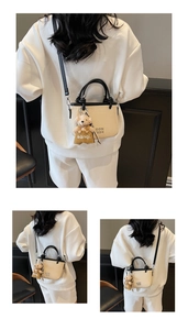 Detail of beige woven bucket bag with black leather straps and a cute plush bear charm