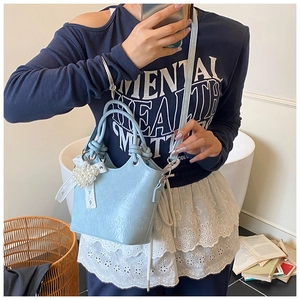 Detail of light blue bucket bag with decorative pearl and lace bow charm on side