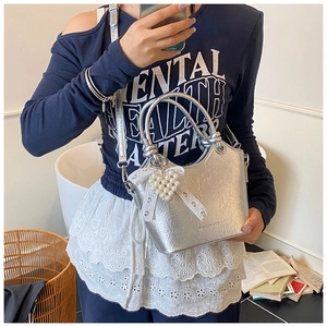 Detail of silver pleated bucket bag with pearl heart charm and lace bow on a model