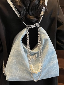 Blue glitter tote bag with chains and butterfly charm worn by a model in dark blazer