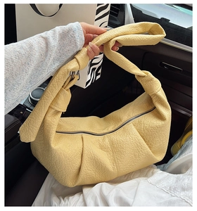 Close-up of the light yellow pleated croissant bag with textured lychee grain faux leather