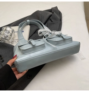 Dettaglio della borsa tote azzurra con tasche frontali e ciondolo a fiocco in pizzo decorativo