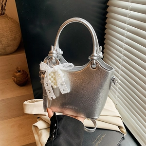 Detail of silver bucket bag with pleated texture, pearl lace bow, and logo branding