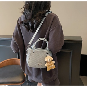 Detail of light blue woven bucket bag with teddy bear charm worn by a model