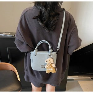 Detail of light blue-grey woven bucket bag with metal logo and bear charm on a model