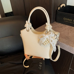 Detailed view of beige bucket bag with lace bow, pearl pendant and leather texture