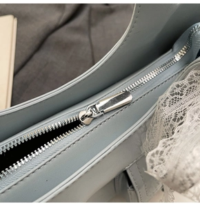 Dettaglio della cerniera in metallo argento e pizzo bianco su borsa in pelle azzurra