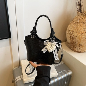 Detail of black glossy bucket bag with lace bow pendant and pearl strap decoration