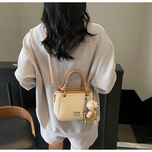 Detail of straw bucket bag with brown leather strap and cute plush bear charm