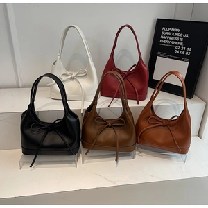 Five minimalist bow-tie underarm tote bags in multiple colors displayed on marble steps