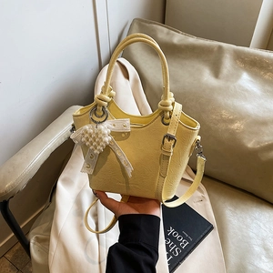 Detail of yellow lychee grain leather bucket bag with pearl heart and lace bow charm