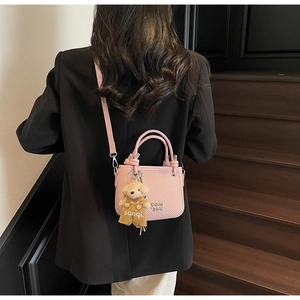 Detailed view of a pink textured bucket bag with metal logo and cute bear pendant