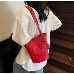Detail of red crocodile pattern bucket bag with brand logo and adjustable shoulder strap