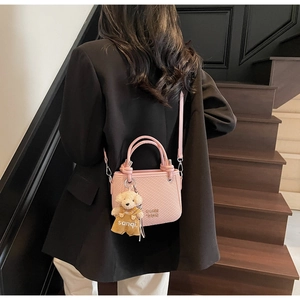 Pink bucket bag with ripple texture and plush bear charm shown in a crossbody style