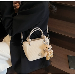 Macro shot of beige woven bucket bag with metal logo detail and cute bear charm