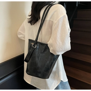 Detail of black crocodile texture bucket bag with silver rings and brand logo