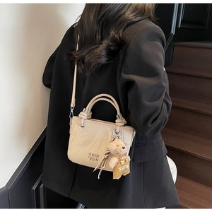 Detail showing beige woven bucket bag with top handle and cute bear charm in use