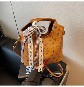 Detail of caramel lychee leather tote showing cute bear prints and a lace bow ribbon