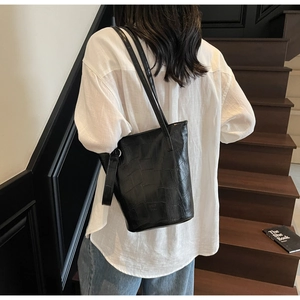 Detail of black crocodile texture bucket bag worn with white shirt and blue denim
