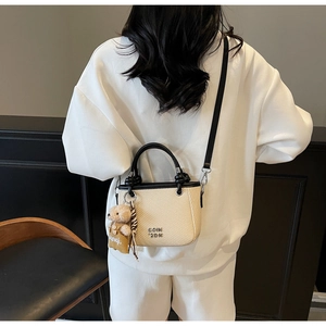 Detail of light beige woven bucket bag with leather trim and cute bear charm accessory
