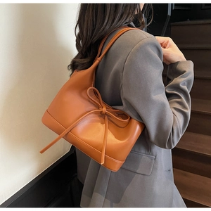 Detailed close-up of a caramel brown leather shoulder bag with a large decorative bow