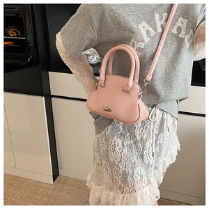 Pink lychee grain leather shell bag with silver hardware worn by a model in a casual setting