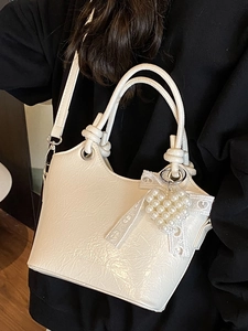 White textured bucket bag with pearl heart charm and adjustable shoulder strap worn by model