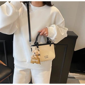 Detail of a chic beige bucket bag featuring black leather trim and a cute teddy bear charm