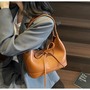 Close-up of caramel leather hobo bag with bow detail worn with a grey blazer