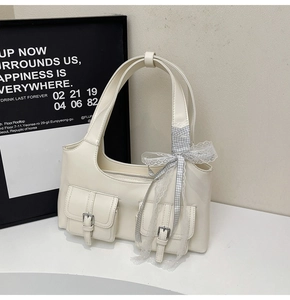 Dettaglio della borsa tote bianco crema con tasche a fibbia e un nastro in pizzo con fiocco