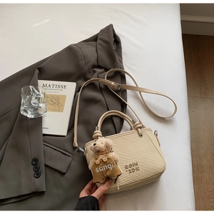Detail of cream crossbody bucket bag with bear charm and textured leather finish