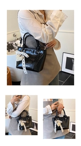Detail of black glossy handbag featuring white ribbon bow and pearl heart charm accessory