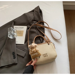 Detailed close-up of woven bucket bag with brown leather strap and teddy bear charm