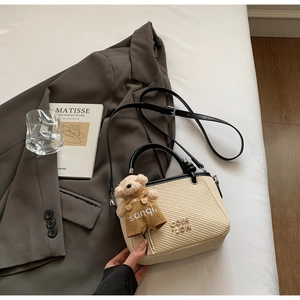 Detailed view of beige woven bucket bag with black leather trim and cute bear charm